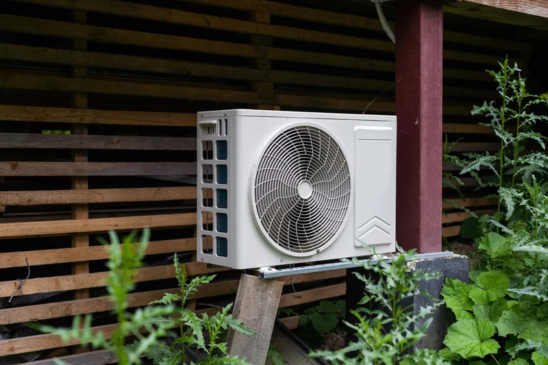 Outdoor HVAC unit installed on a wooden platform surrounded by greenery.