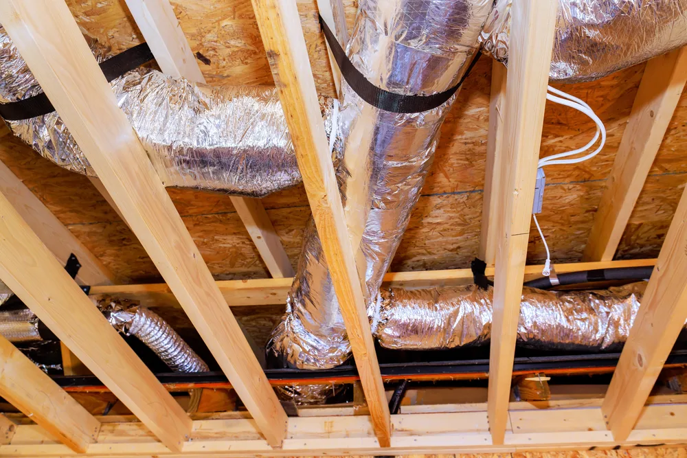 Silver HVAC ductwork runs between wooden beams in a ceiling.