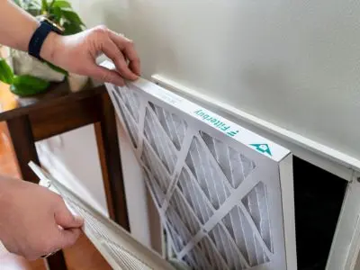 Person replacing an HVAC air filter, demonstrating the importance of regular air filter maintenance for indoor air quality and HVAC efficiency.