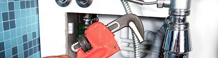 Plumber using adjustable wrench on plumbing fixtures, showcasing RupCoe Plumbing's expertise in maintenance and repairs.