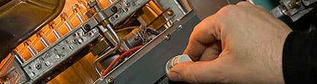 Hand adjusting a control knob on a heating system, illustrating maintenance and repair services for plumbing and heating by RupCoe Plumbing, Heating & Air Conditioning.