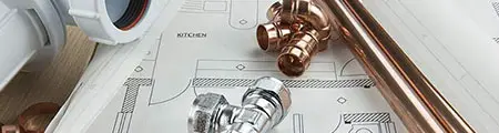 Plumbing materials including copper pipes, fittings, and a blueprint for kitchen plumbing, highlighting RupCoe Plumbing's expertise in plumbing services.