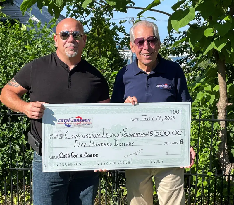 Cotti-Johnson HVAC representatives presenting a $500 check to the Concussion Legacy Foundation, supporting awareness and research for CTE, with a backdrop of greenery.