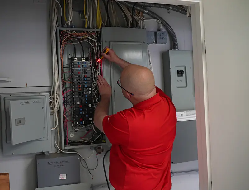 Electrician inspecting circuit breaker panel with multimeter, ensuring electrical safety and functionality for HVAC services in Taunton, MA.