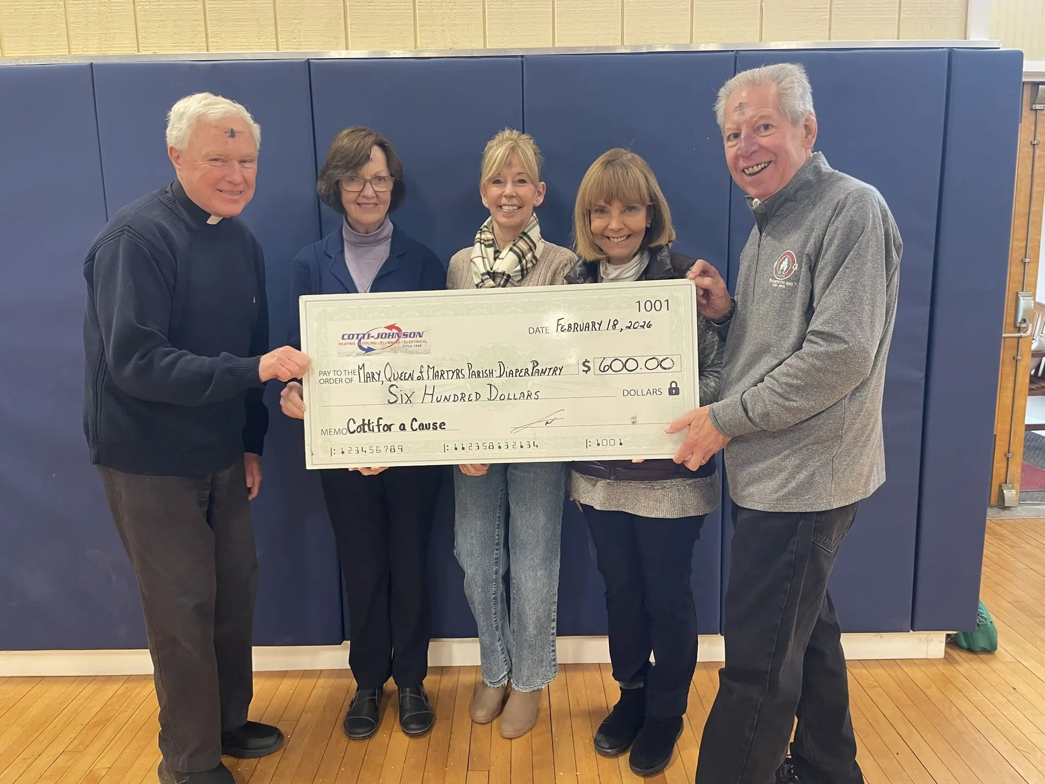 Group presenting a large check for $600 to support the Diaper Pantry at Saint Kateri Church, featuring members of Cotti Johnson HVAC, Inc. and local community leaders, in a gymnasium setting.