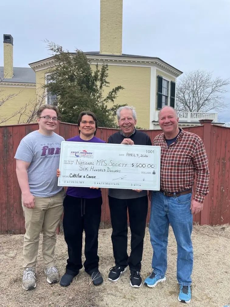 Group of four individuals holding a large check for $600 made out to the National MPS Society, with a "Cotti for a Cause" logo, in a community setting.