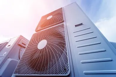 Air conditioning unit with dual fans against a blue sky, emphasizing HVAC maintenance and efficiency for warmer months.