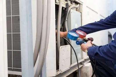 HVAC technician using gauges to service an air conditioning unit, highlighting maintenance for home comfort.