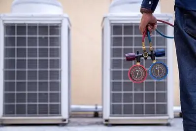 HVAC technician holding pressure gauges in front of outdoor air conditioning units, emphasizing air conditioning maintenance and repair services.