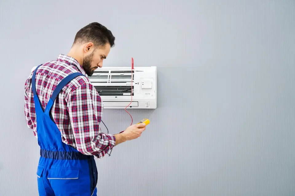 HVAC technician inspecting air conditioning unit with multimeter in hand, highlighting air conditioning maintenance for optimal performance.
