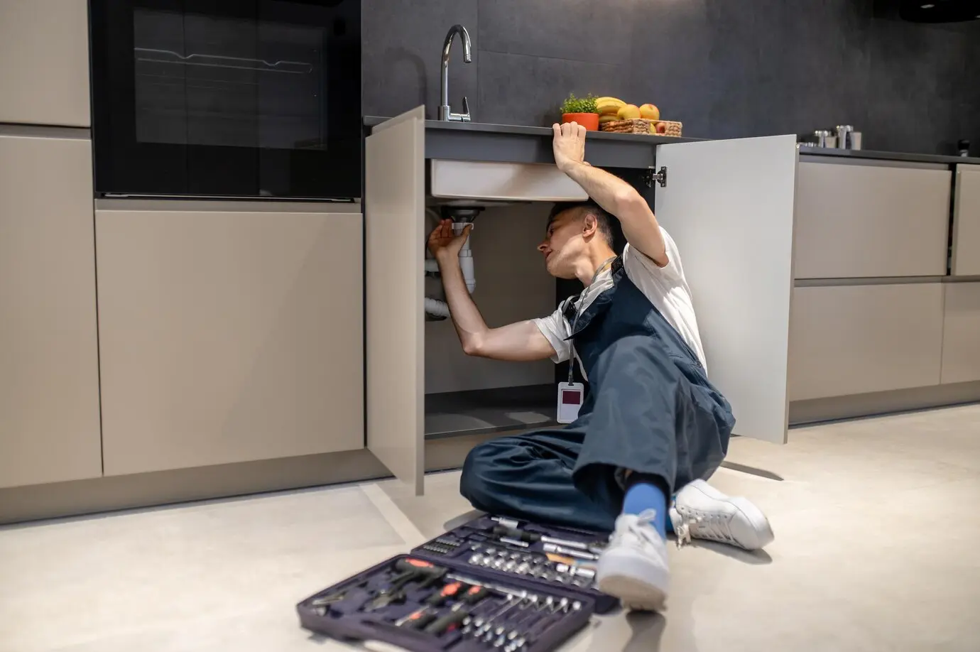Plumber performing maintenance under a kitchen sink with tools nearby, emphasizing plumbing efficiency and home system care.
