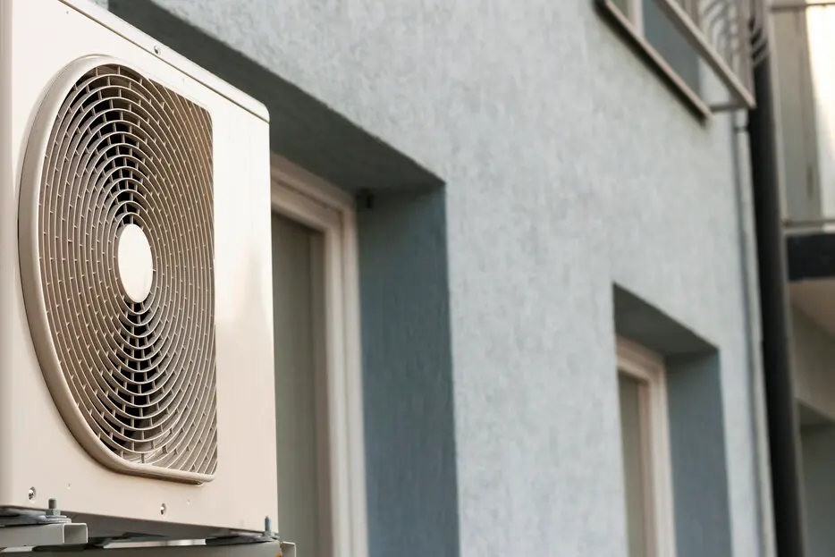 Heat pump unit mounted on exterior wall, highlighting energy-efficient heating and cooling solution for homes.