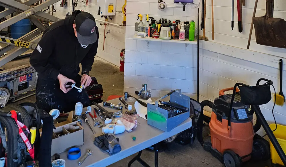 Plumber working on plumbing components at a workbench with tools and equipment in a commercial setting.