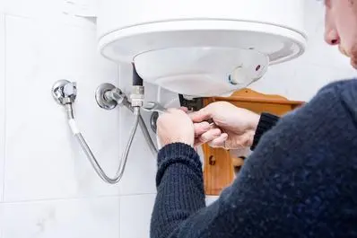 Person repairing a water heater, focusing on connection points and tools, highlighting maintenance for home comfort during cooler months.