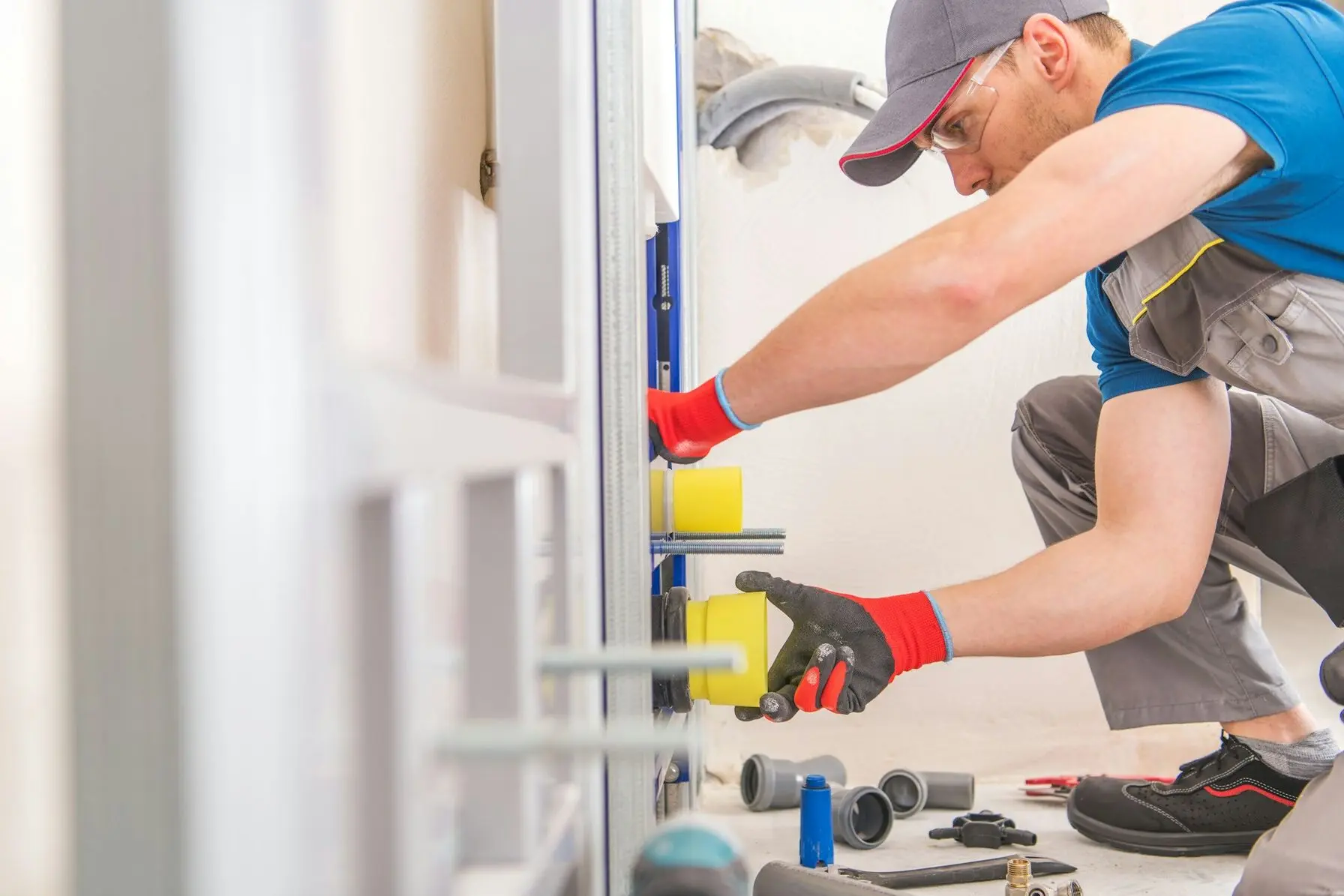 Plumber in gloves working on plumbing installation with tools and pipes in a home setting, emphasizing the importance of timely plumbing maintenance to prevent water damage and ensure safety.