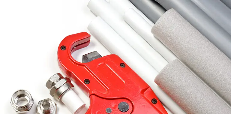 Red pipe cutter with various PVC and copper pipes, plumbing fittings, and insulation materials, illustrating tools used for repiping services by Jim Wagner Plumbing.