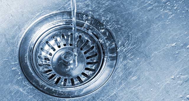 Close-up of a kitchen sink drain with water flowing, illustrating drain cleaning services by Jim Wagner Plumbing in Lisle, IL.