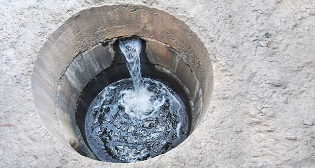 Flood control sewer drain system with flowing water, showcasing a flapper valve in a circular manhole, relevant to plumbing services in Naperville and Elmhurst, IL.