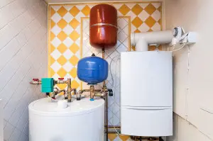 Hot water heater system with blue and red expansion tanks, plumbing connections, and wall-mounted exhaust, illustrating components relevant to water heater maintenance and repair.