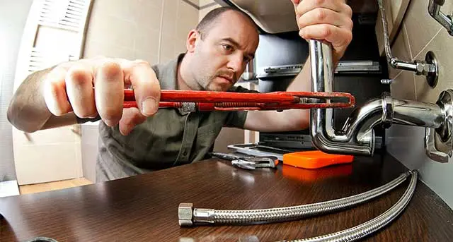 Plumber using a wrench to repair sink plumbing, showcasing emergency plumbing service expertise for urgent issues.