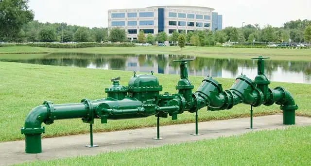 Green backflow prevention assembly installed near a water source, emphasizing plumbing safety and compliance, relevant to Jim Wagner Plumbing's backflow testing and installation services in Elmhurst, IL.