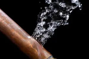 Burst copper pipe spraying water, illustrating a plumbing emergency scenario relevant to homeowner plumbing issues.