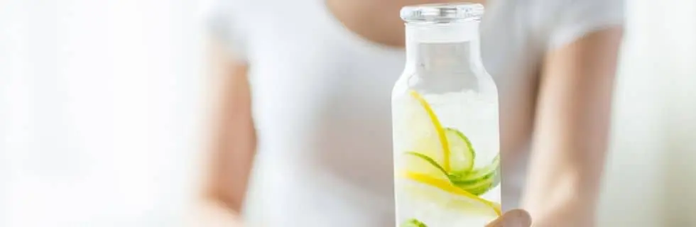 Person holding a glass bottle of infused water with lemon and lime slices, emphasizing the importance of filtered water for refreshing beverages like lemonade.