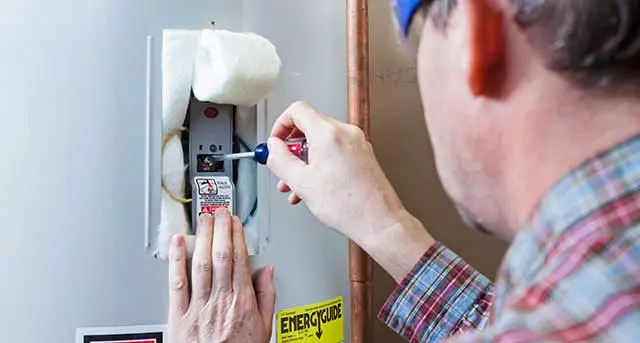 Technician performing maintenance on a commercial water heater, adjusting the thermostat with a screwdriver, showcasing Jim Wagner Plumbing's repair services.
