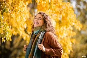 Joyful woman in a scarf and coat standing outside in the fall