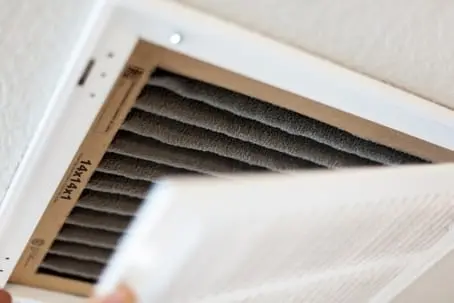 Close-up view of an AC technician changing a dirty, pleated HVAC air filter in a ceiling vent in Hemet, CA.