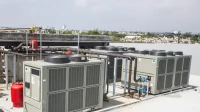 Rooftop HVAC units with pipes and a fire extinguisher, overlooking the distant cityscape of Hemet, California, under a partly cloudy sky.