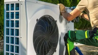 Technician in a green uniform servicing or installing a large outdoor air conditioning unit as part of an AC maintenance routine in Hemet, CA.