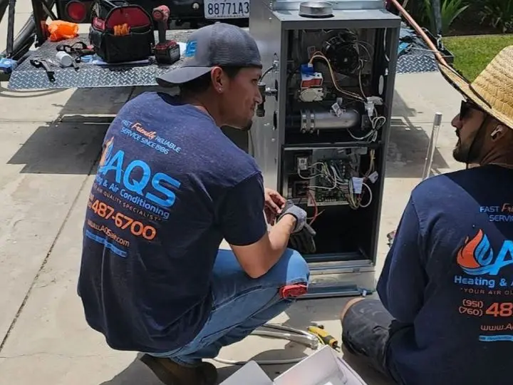 Technicians from AQS Heating & Air Conditioning performing maintenance on a ductless mini-split system, emphasizing HVAC service expertise in Hemet, CA.