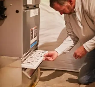 Man replacing an air filter in an HVAC system, emphasizing the importance of regular maintenance for optimal performance and efficiency.