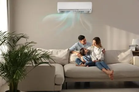 Family enjoying cool air from an energy-efficient air conditioner while relaxing on a sofa in a well-lit living room, emphasizing comfort and HVAC efficiency.