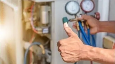 An AC technician's hand giving a thumbs up while holding HVAC gauges near an air conditioning unit during routine AC maintenance in California.