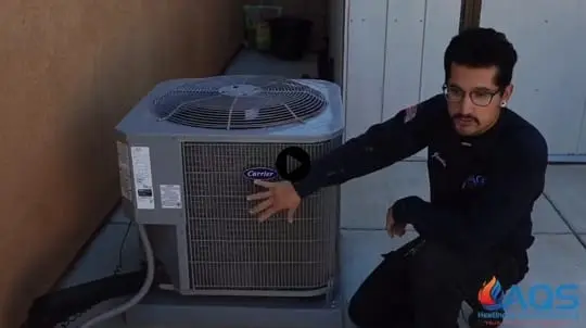 A technician inspects an outdoor air conditioning unit next to a house in California, with the AQS logo visible on his uniform, showcasing expert local HVAC repair.