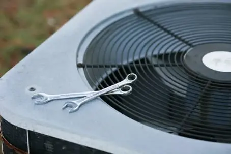 Two wrenches lying on top of an outdoor air conditioning unit's fan highlight the tools essential for thorough AC maintenance.