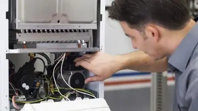 A local HVAC repair technician is diligently inspecting and working on the internal components of an industrial machine in California.