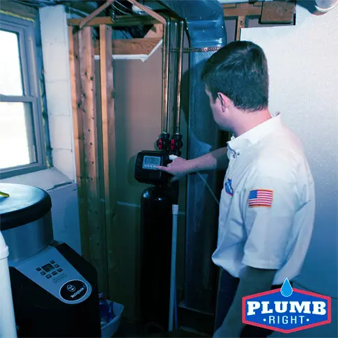 Plumber from Plumb Right working on a water filtration system with pipes and control display in a bright room.
