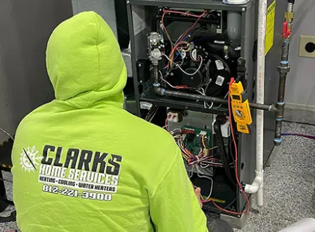 Technician in green hoodie servicing HVAC equipment at Clark's Home Services in industrial setting with tools and pipes.