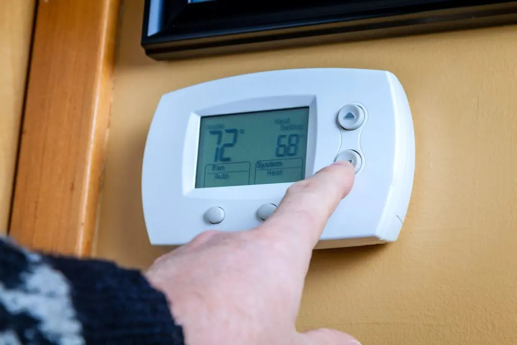 Hand adjusting a digital thermostat displaying 72°F inside temperature and 68°F heat setting, relevant to HVAC system settings and energy efficiency.