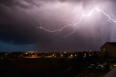 Lightning striking during a storm over a suburban landscape, illustrating the importance of surge protection for home electronics.