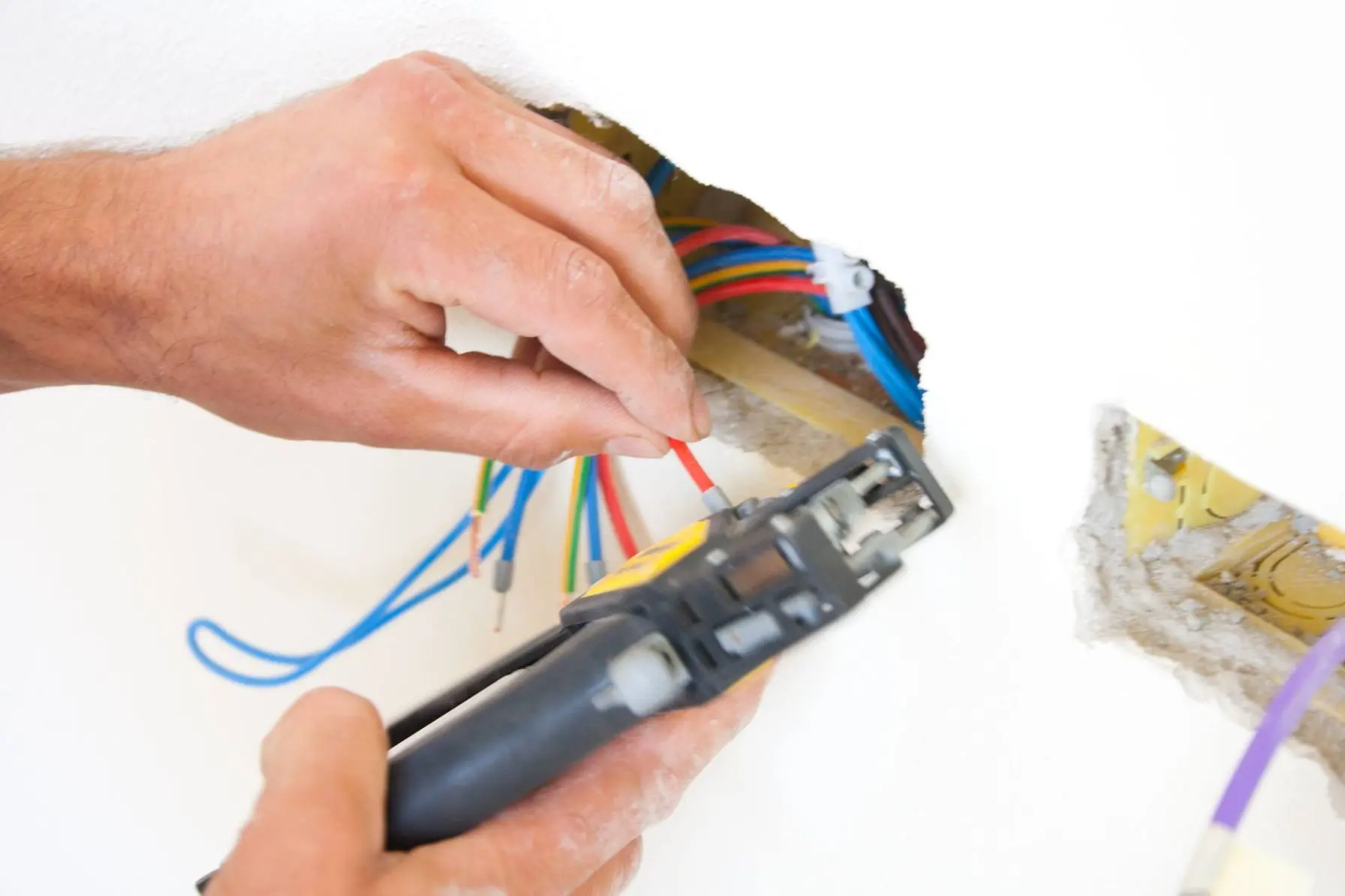Hands using a wire stripper on electrical wires inside a wall, illustrating electrical maintenance and installation relevant to HVAC and indoor air quality services.