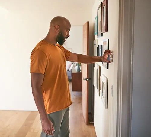 Man adjusting a thermostat, highlighting HVAC maintenance for homes by Acosta Heating, Cooling & Electrical.