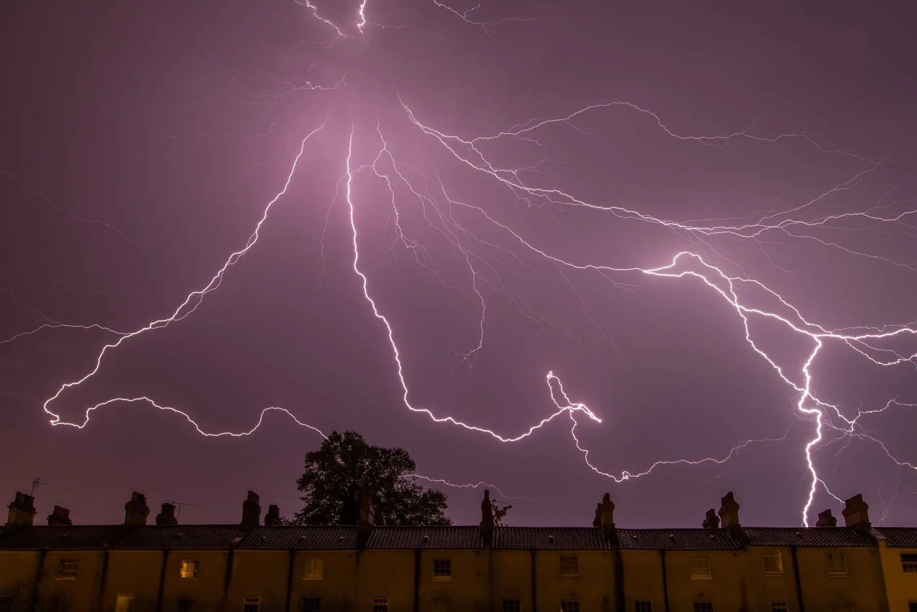 Lightning striking in a stormy sky above residential rooftops, illustrating potential HVAC challenges during severe weather.