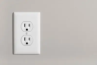 White electrical outlet installed on a light gray wall, illustrating safe electrical installation relevant to surge protection and outdoor electrical solutions.