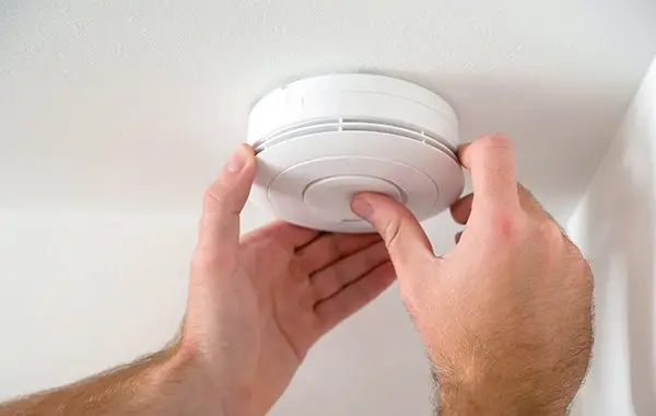 White smoke detector installed on ceiling, highlighting home safety by Acosta Heating, Cooling & Electrical.