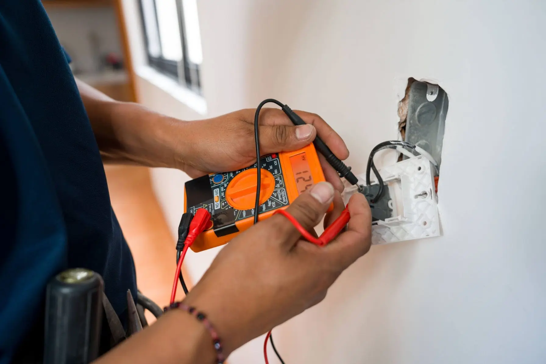 Electrician using a multimeter to test electrical outlet connections in a residential setting, emphasizing HVAC and electrical service expertise in Charlotte, NC.