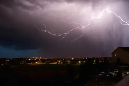 Lightning striking during a storm over a suburban landscape, illustrating the importance of surge protection for home electronics.